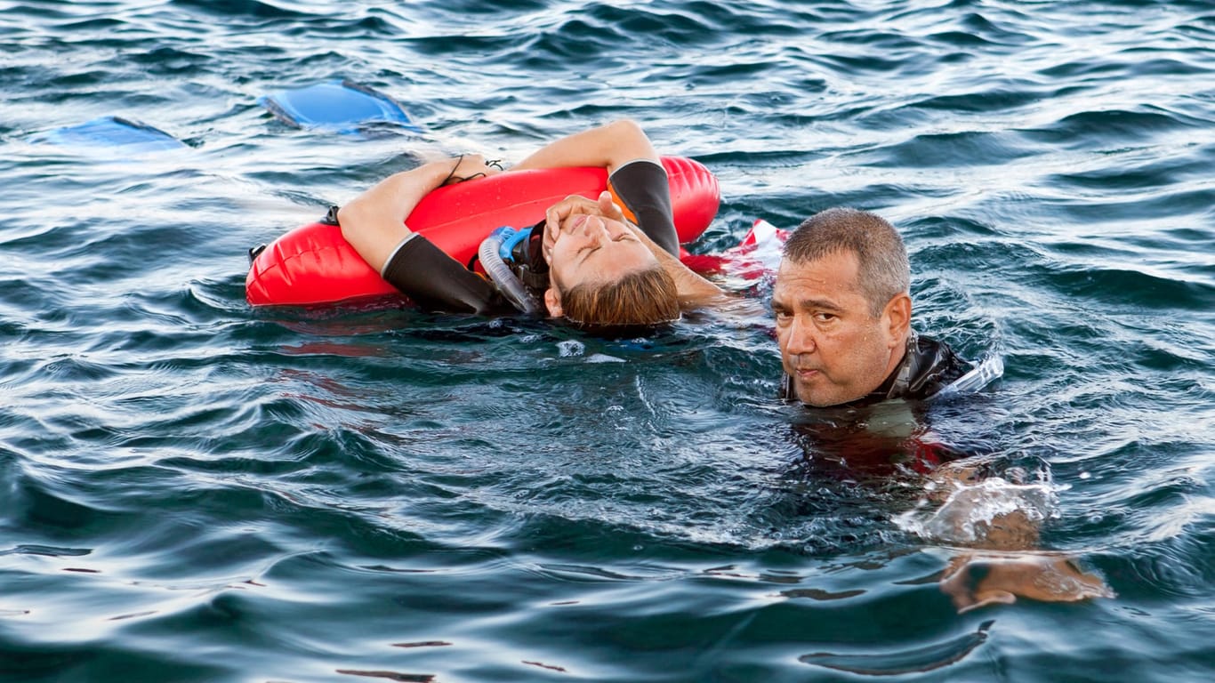 Rettung: Der Rettungsschwimmer hält den Kopf der Person über Wasser, während diese sich an der Boje festhält.
