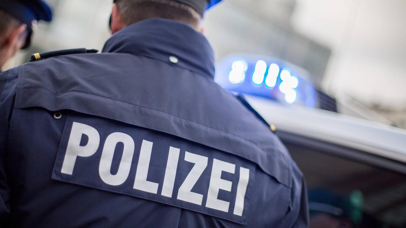 Ein Beamter der Polizei Nordrhein-Westfalen steht vor einem Streifenwagen (Symbolbild): Noch ist die Ursache eines tödlichen Autounfalls in Essen nicht zweifelsfrei geklärt.