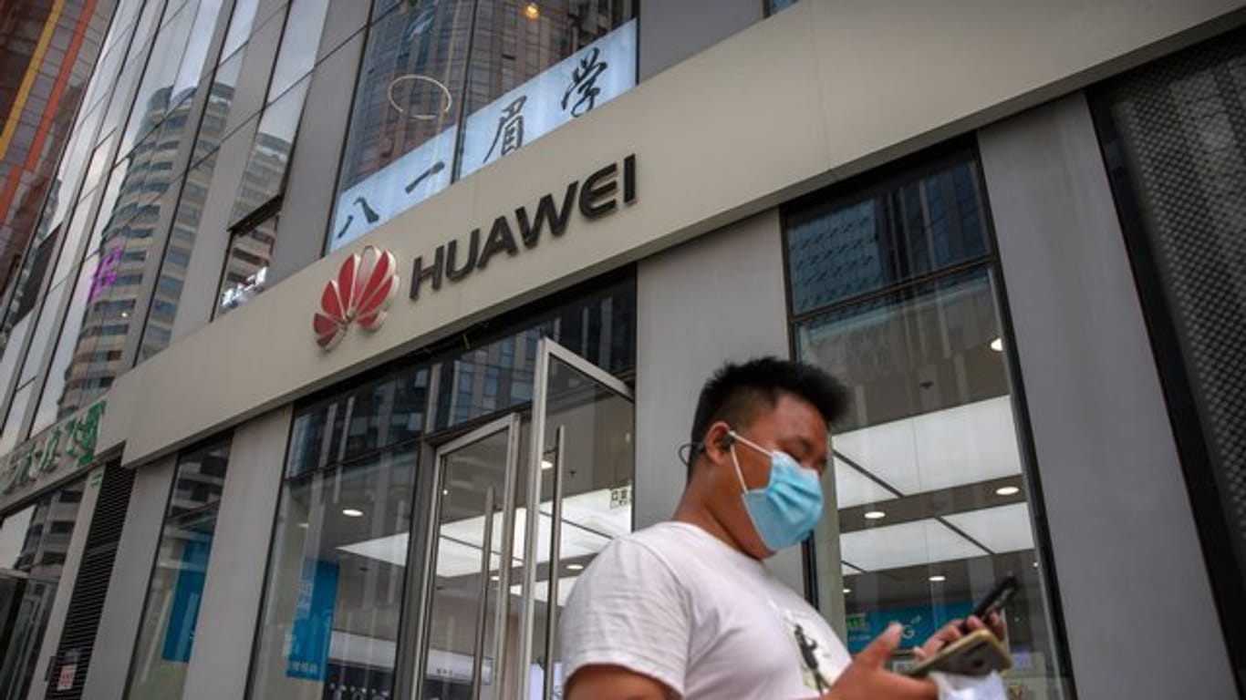 Ein Mann mit Gesichtsmaske schaut auf sein Smartphone, als er an einem Huawei-Laden in Peking vorbeigeht.