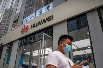 Ein Mann mit Gesichtsmaske schaut auf sein Smartphone, als er an einem Huawei-Laden in Peking vorbeigeht.