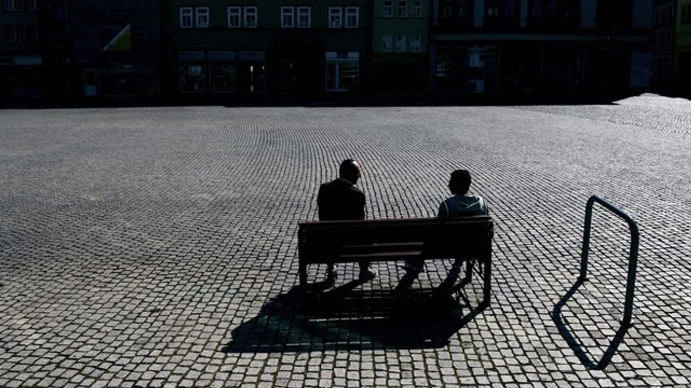 Zwei Menschen sitzen auf dem leeren Marktplatz auf einer Bank