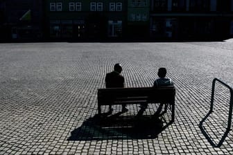 Zwei Menschen sitzen auf dem leeren Marktplatz auf einer Bank