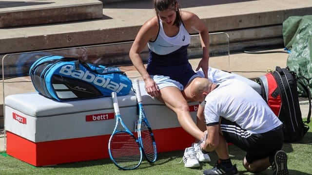 Julia Görges (l) wird am umgeknickten Fuß von einem Therapeuten behandelt.