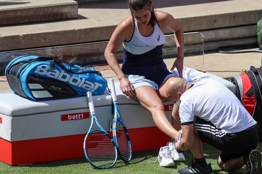 Julia Görges (l) wird am umgeknickten Fuß von einem Therapeuten behandelt.