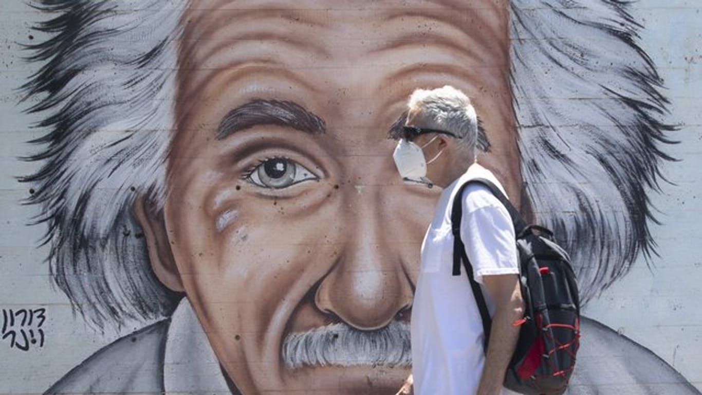 Ein israelischer Mann, der einen Mund- und Nasenschutz trägt, geht an einem Wandbild vorbei, das Albert Einstein zeigt.