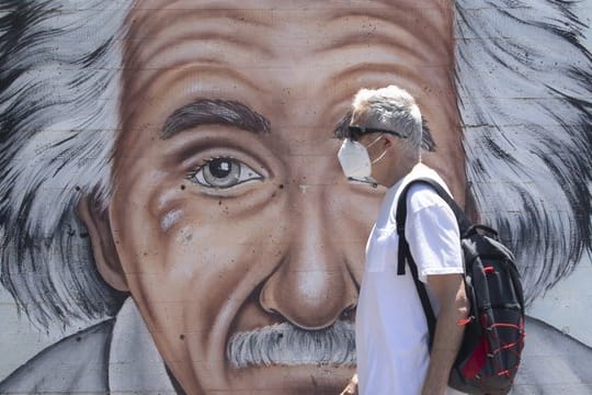 Ein israelischer Mann, der einen Mund- und Nasenschutz trägt, geht an einem Wandbild vorbei, das Albert Einstein zeigt.