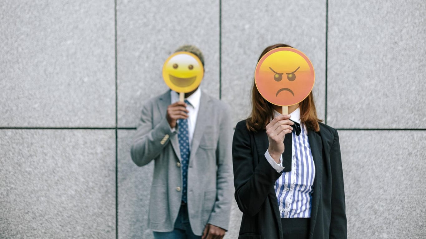 Ein Mann und eine Frau halten ein Emoji vors Gesicht: Eine exklusive Umfrage von t-online.de zeigt, wie die Deutschen zu Emojis stehen.