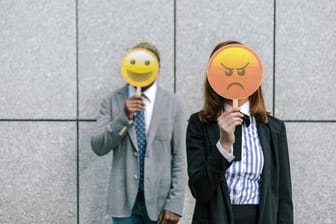 Ein Mann und eine Frau halten ein Emoji vors Gesicht: Eine exklusive Umfrage von t-online.de zeigt, wie die Deutschen zu Emojis stehen.