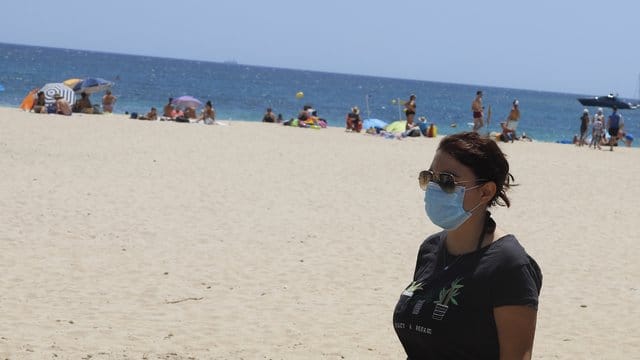 Eine junge Frau mit einer Schutzmaske an einem Strand.