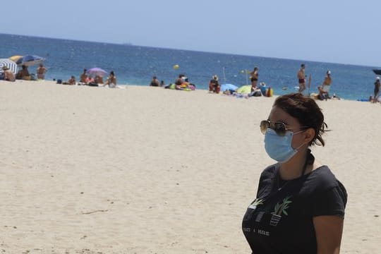 Eine junge Frau mit einer Schutzmaske an einem Strand.