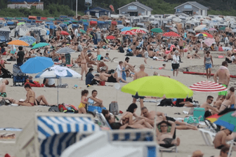Viele Menschen liegen am Strand mit Sonnenschirmen und Strandkörben: Die Küstenregionen in Deutschland sind gut besucht.