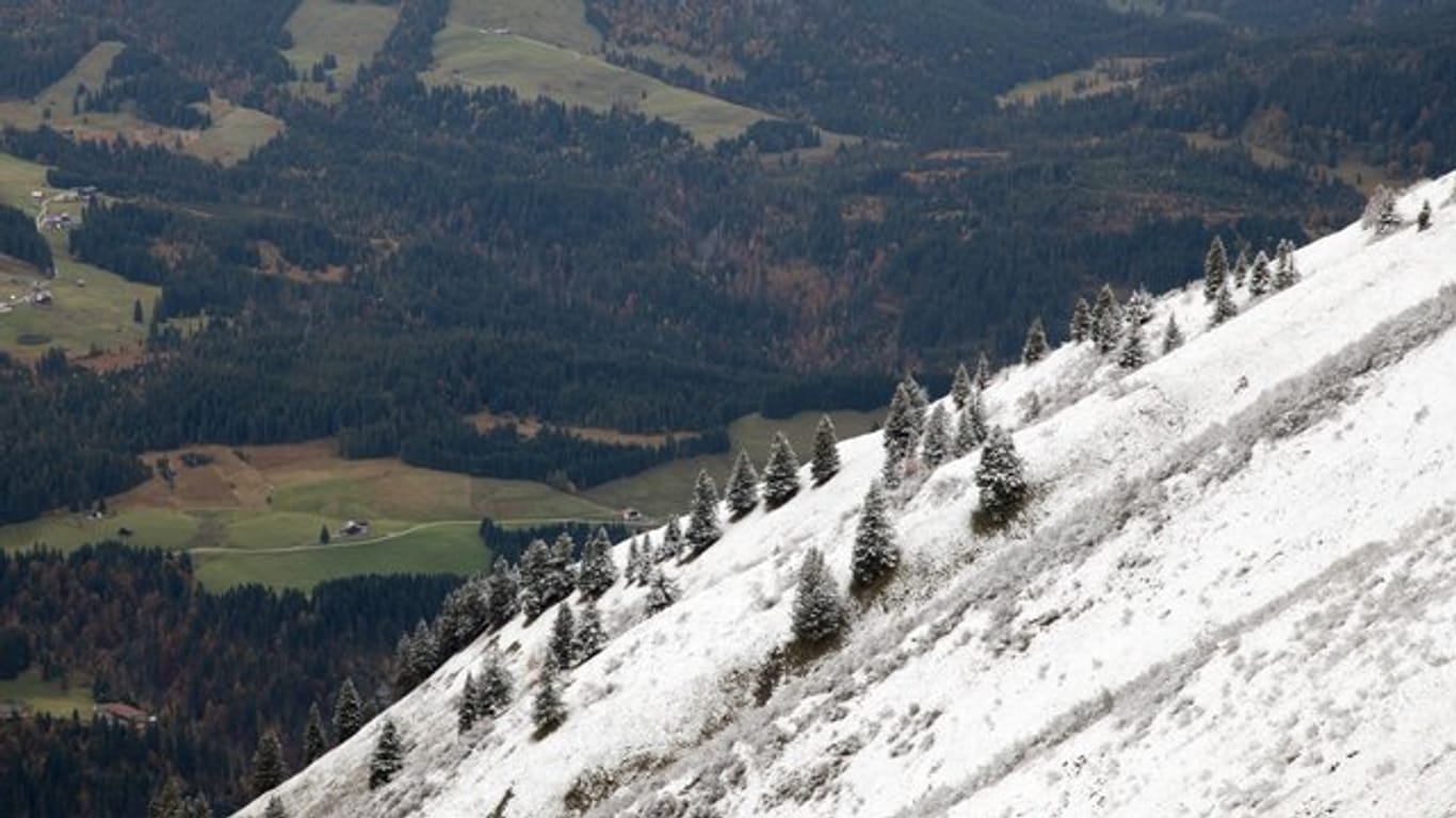 Ein mit etwas Schnee bedeckter Hang vor grünen Wiesen im Tal.