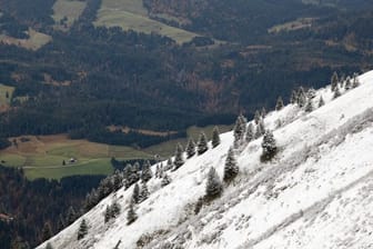 Ein mit etwas Schnee bedeckter Hang vor grünen Wiesen im Tal.