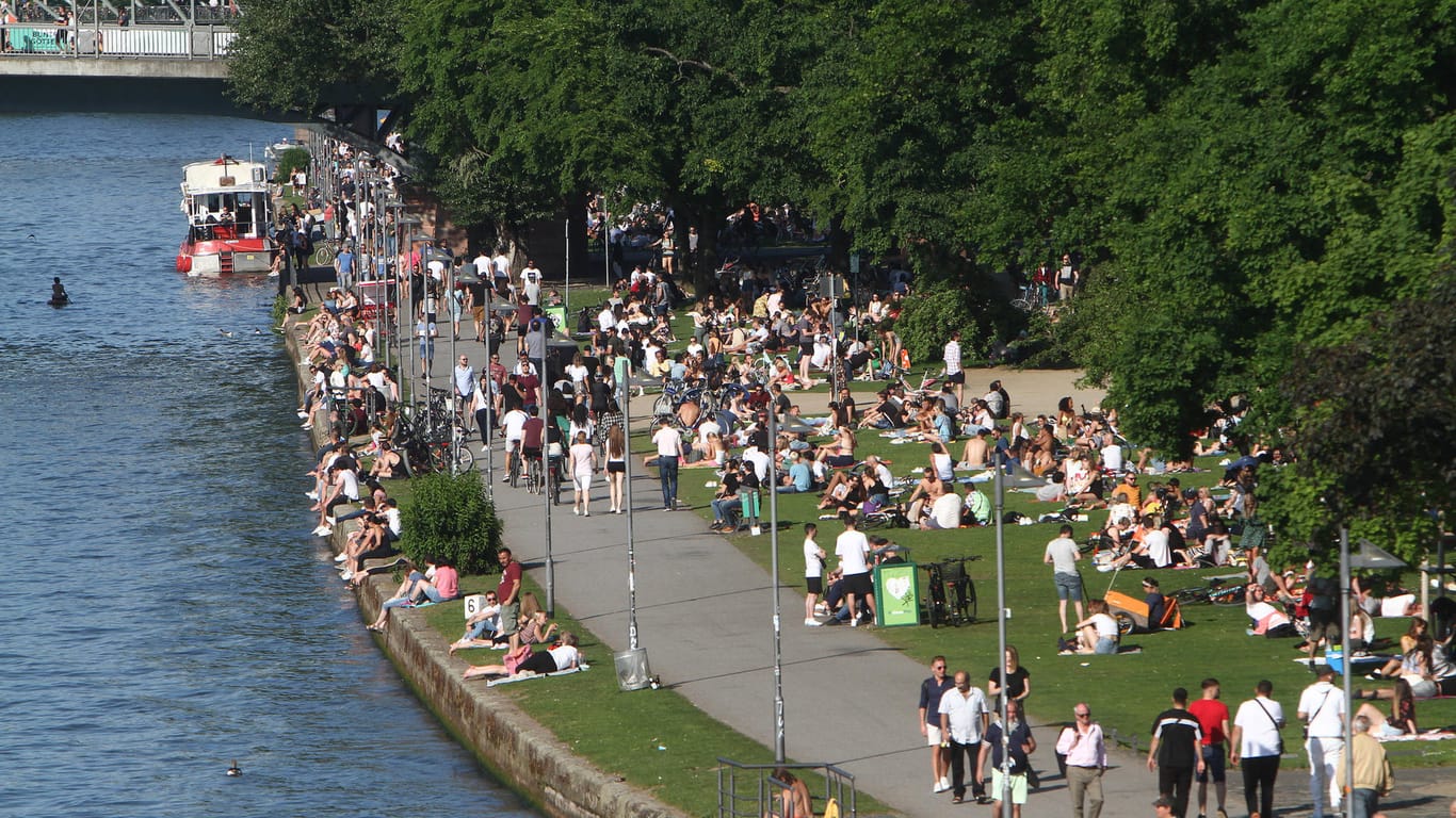Menschen sitzen und feiern am Mainufer (Archivbild vom Mai): In Frankfurt sollen jetzt ausgewiesene Partyzonen entstehen