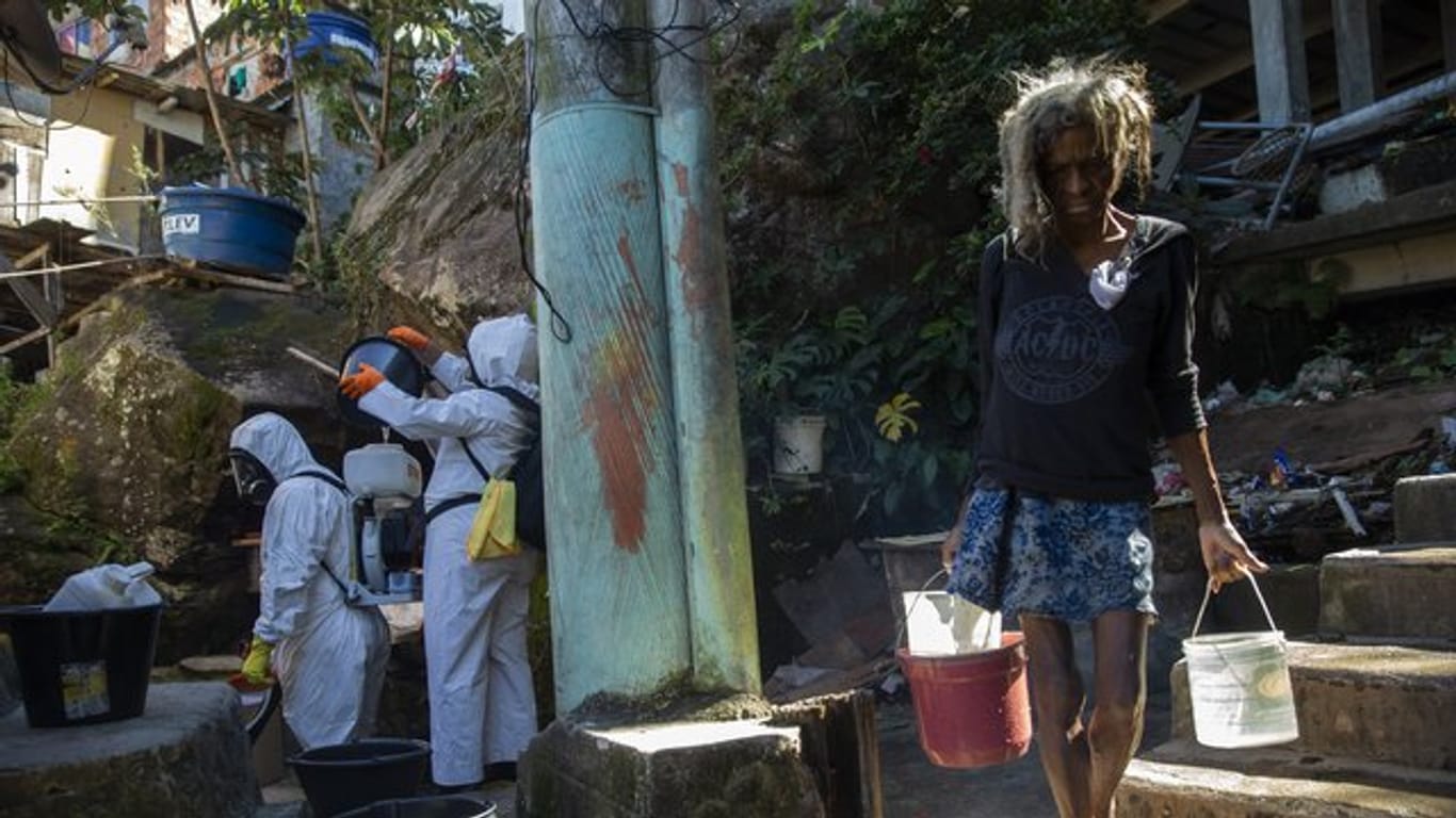 Eine Bewohnerin in einer Favela in Rio de Janeiro holt Wasser, während Freiwillige versuchen das Viertel zu desinfizieren.