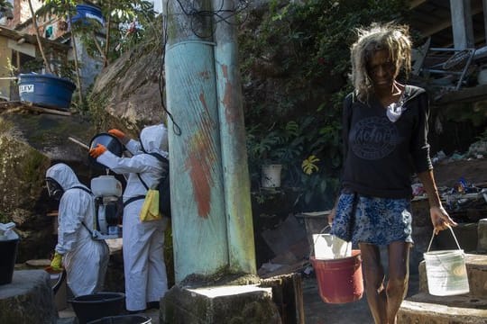 Eine Bewohnerin in einer Favela in Rio de Janeiro holt Wasser, während Freiwillige versuchen das Viertel zu desinfizieren.