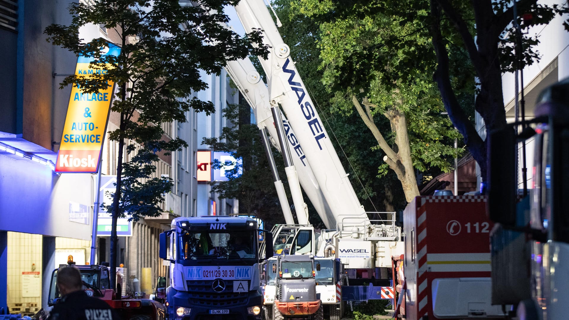 Zwei Kräne stehen auf einer Straße vor einem Haus, in dessen Hinterhof ein Gebäude eingestürzt ist: Sie sollen bei der Suche nach einem noch immer vermissten Arbeiter helfen.