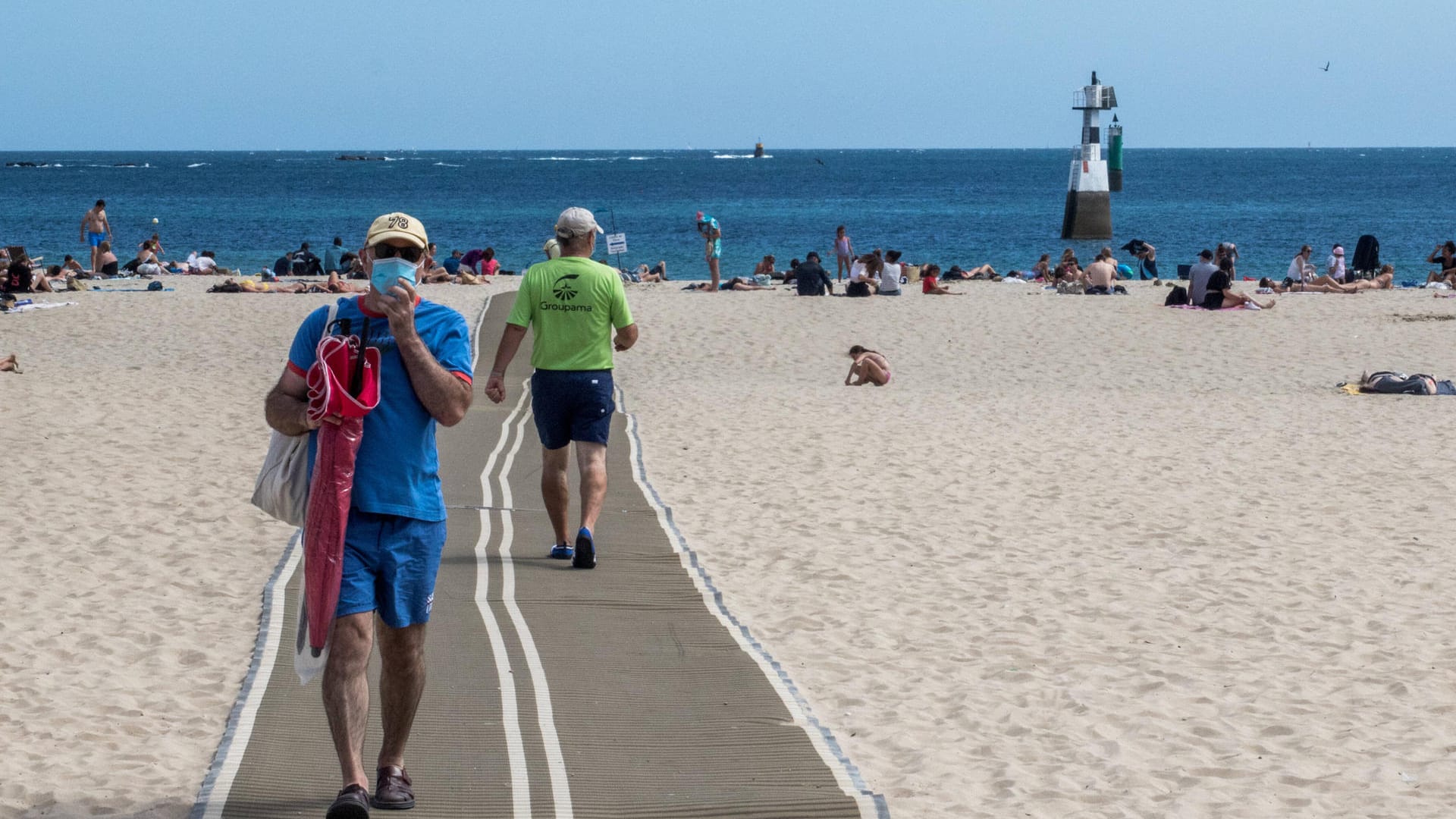 Ein Urlauber am Strand mit Mundschutz (Symbolbild): In Karlsruhe hat die Stadt an die Bürger appelliert, beim Reisen vorsichtig zu bleiben.