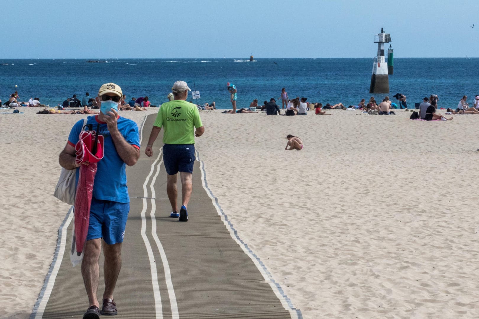 Ein Urlauber am Strand mit Mundschutz (Symbolbild): In Karlsruhe hat die Stadt an die Bürger appelliert, beim Reisen vorsichtig zu bleiben.