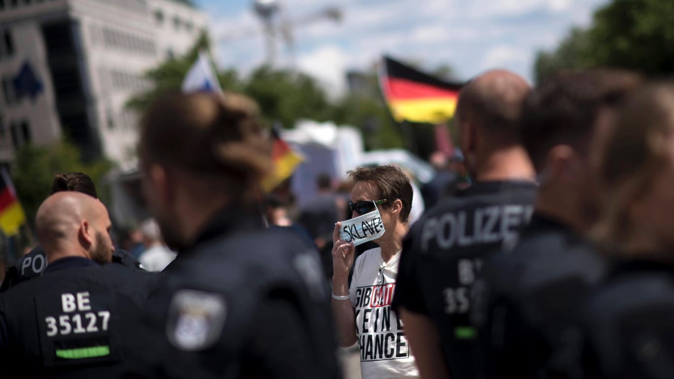 Eine Corona-Gegnerin steht hinter Polizisten in Berlin: Ein Bündnis aus Corona-Leugnern hat zu einer großen Demonstration in Berlin eingeladen. Ob viele Teilnehmer kommen, ist aber fraglich.