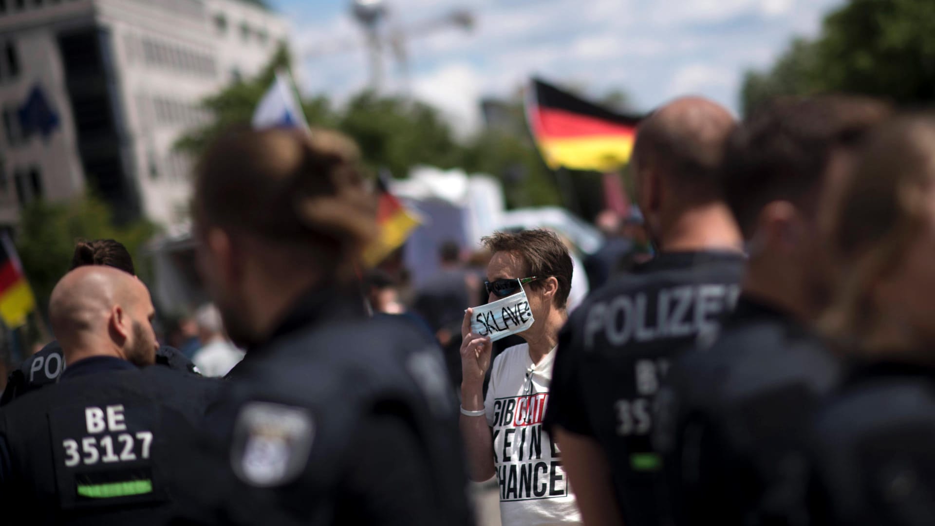 Eine Corona-Gegnerin steht hinter Polizisten in Berlin: Ein Bündnis aus Corona-Leugnern hat zu einer großen Demonstration in Berlin eingeladen. Ob viele Teilnehmer kommen, ist aber fraglich.