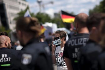Eine Corona-Gegnerin steht hinter Polizisten in Berlin: Ein Bündnis aus Corona-Leugnern hat zu einer großen Demonstration in Berlin eingeladen. Ob viele Teilnehmer kommen, ist aber fraglich.