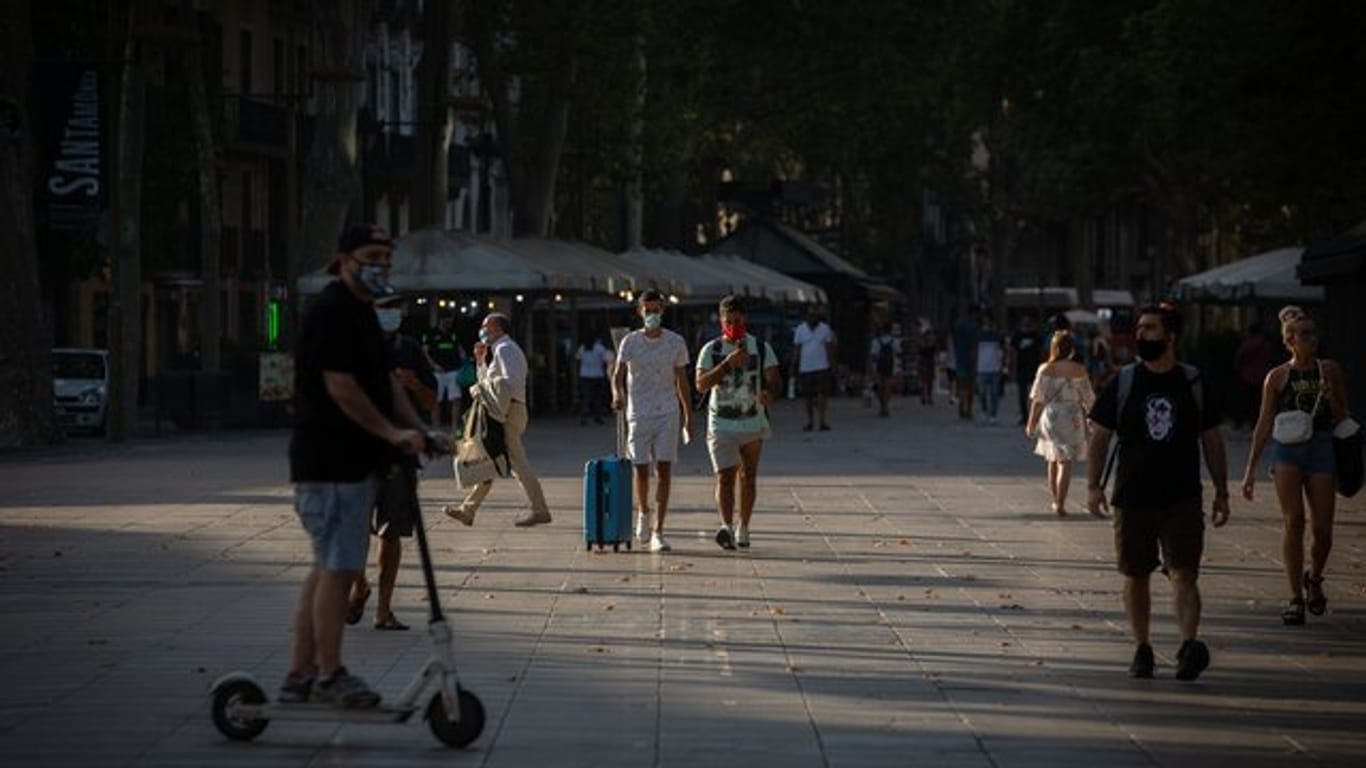 Menschen, manche von ihnen mit Mundschutz, gehen auf der langen Promenade La Rambla in Barcelona entlang.