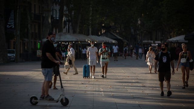 Menschen, manche von ihnen mit Mundschutz, gehen auf der langen Promenade La Rambla in Barcelona entlang. Menschen, manche von ihnen mit Mundschutz, gehen auf der langen Promenade La Rambla in Barcelona entlang.