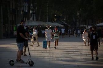 Menschen, manche von ihnen mit Mundschutz, gehen auf der langen Promenade La Rambla in Barcelona entlang.