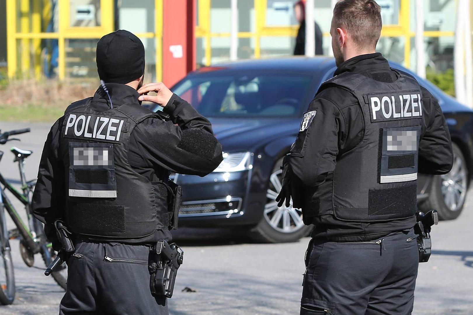 Zwei Polizisten mit schusssicheren Westen stehen vor einem Pkw (Symbolbild): In Karlsruhe sind zwei Polizisten verletzt worden.