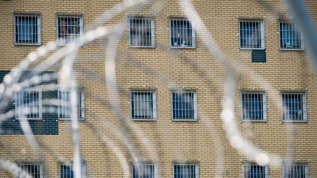 Die Fenster einer JVA sind hinter Stacheldrahtzaun zu sehen