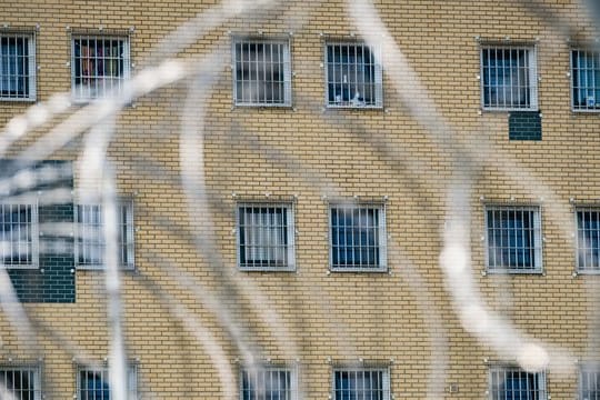 Die Fenster einer JVA sind hinter Stacheldrahtzaun zu sehen