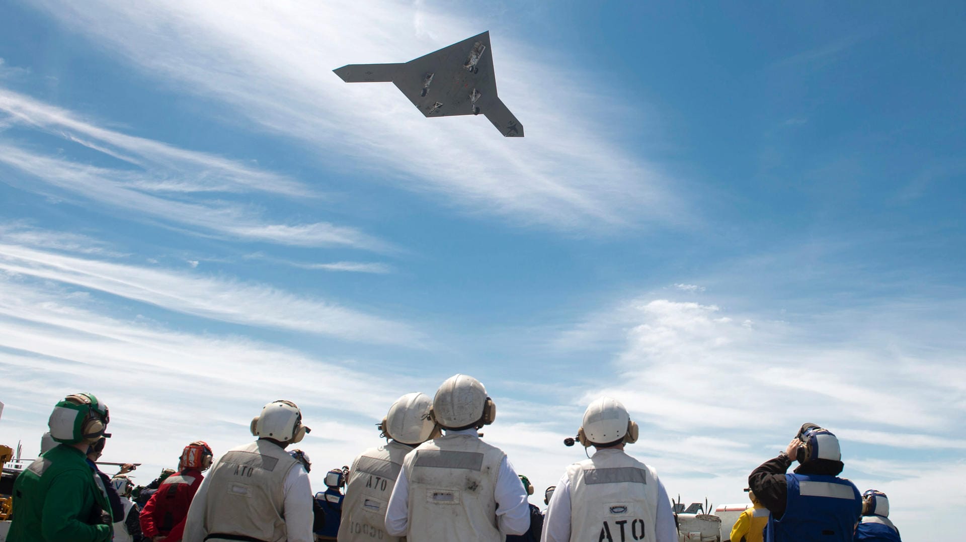 Braucht keinen Piloten: Besatzungsmitglieder des Flugzeugträgers USS George H.W. Bush beobachten eine unbemannte X-47B Kampfdrohne beim Überflug. Das Fluggerät ist in der Lage, halbautonome Einsätze zu fliegen.