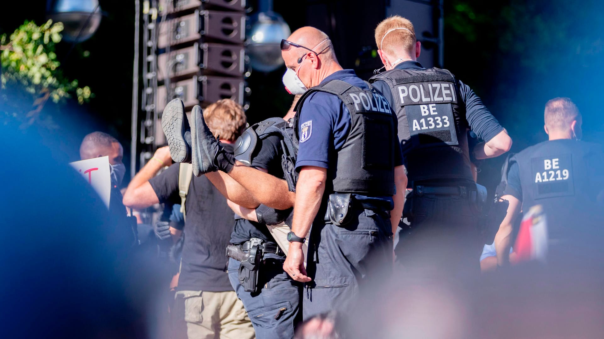 Polizisten tragen bei der Kundgebung gegen die Corona-Beschränkungen auf der Straße des 17. Juni eine Person von der Bühne.