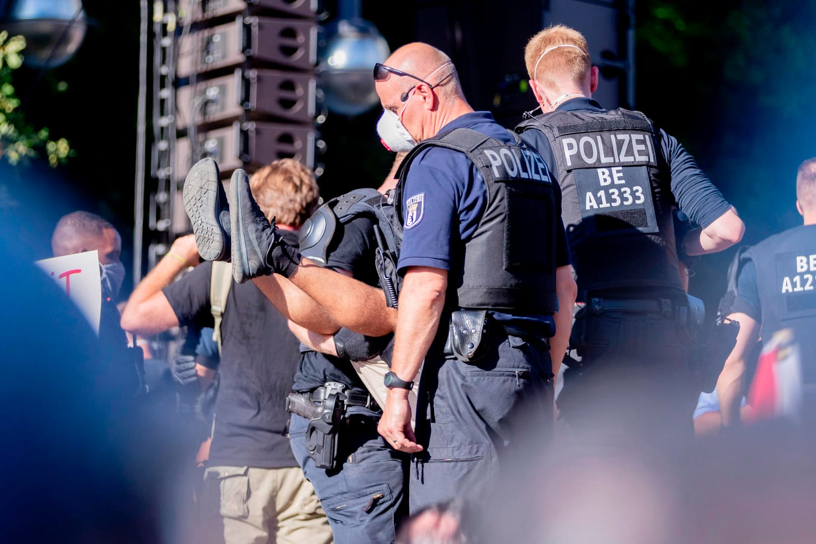 Polizisten tragen bei der Kundgebung gegen die Corona-Beschränkungen auf der Straße des 17. Juni eine Person von der Bühne.