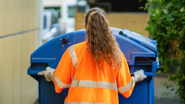 Die Studentin Laura schiebt eine Papierabfalltonne zum Abfallsammelfahrzeug.