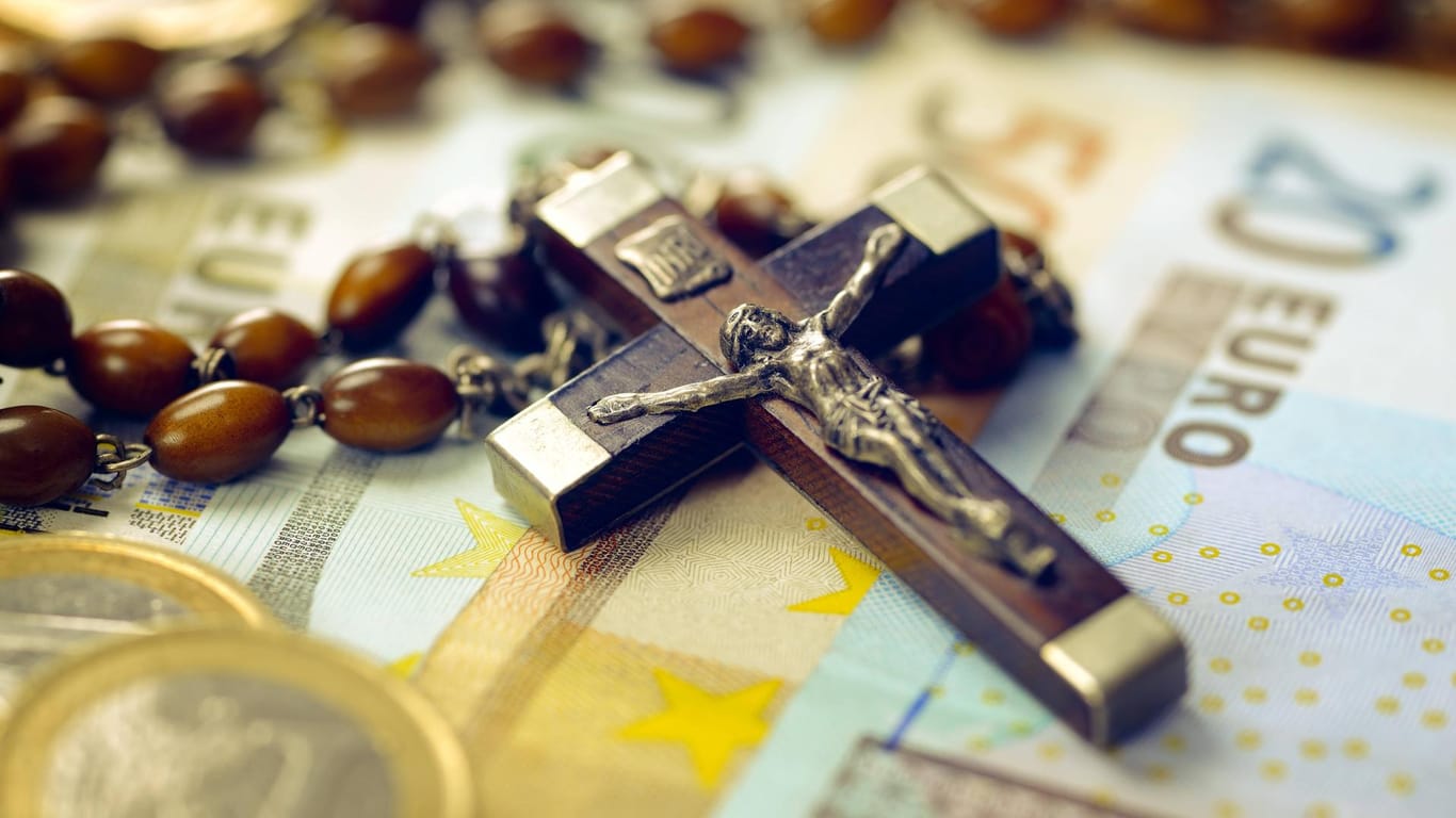 Kreuz mit Rosenkranz auf Geldscheinen: Menschen finden die skurrilsten Gründe, um die Kirchensteuer nicht abzuführen.