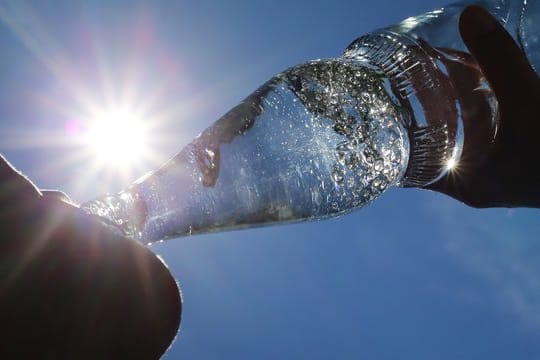 Eine Frau trinkt aus einer Flasche sprudelndes Mineralwasser.