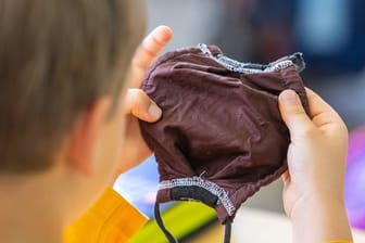 Ein Schüler hält im Klassenzimmer einen Mundschutz in den Händen: Eine Pflicht zum Tragen einer Maske soll es nicht geben.