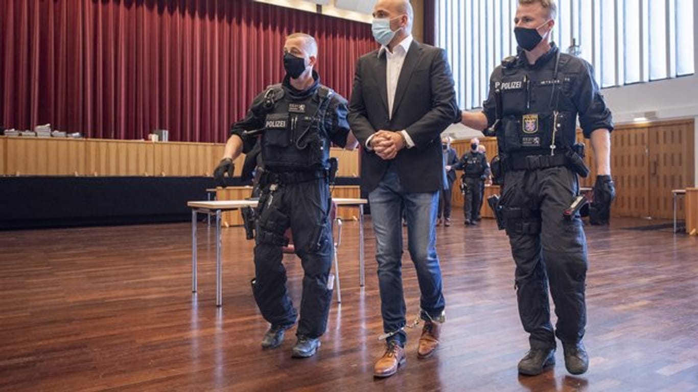 An Händen und Füßen gefesselt ist einer der Hauptangeklagten, den bewaffnete Polizisten in die zu einem Gerichtssaal umfunktionierte Kongresshalle in Gießen bringen.