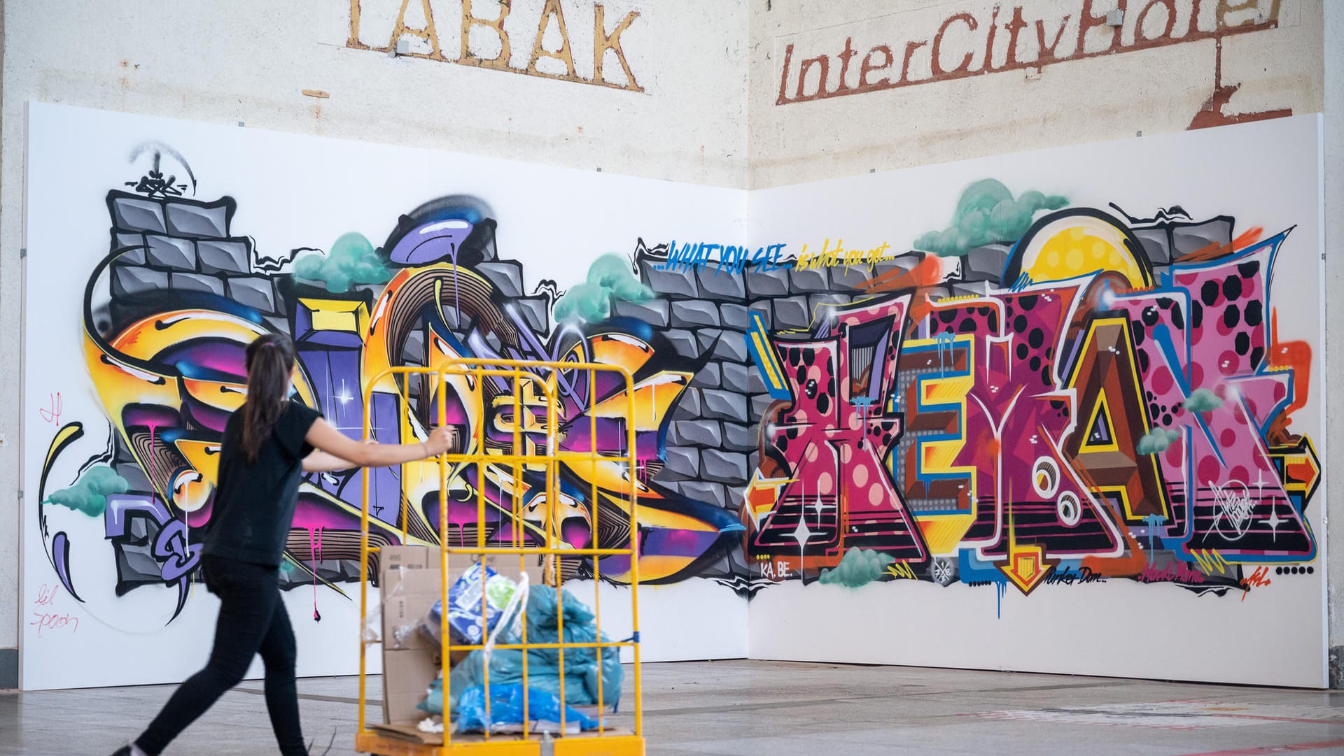 Eine Frau geht an einem Graffiti vorbei. Über dem Werk hängen noch die Überreste der Beschriftungen "Tabak" und "Inter City Hotel".