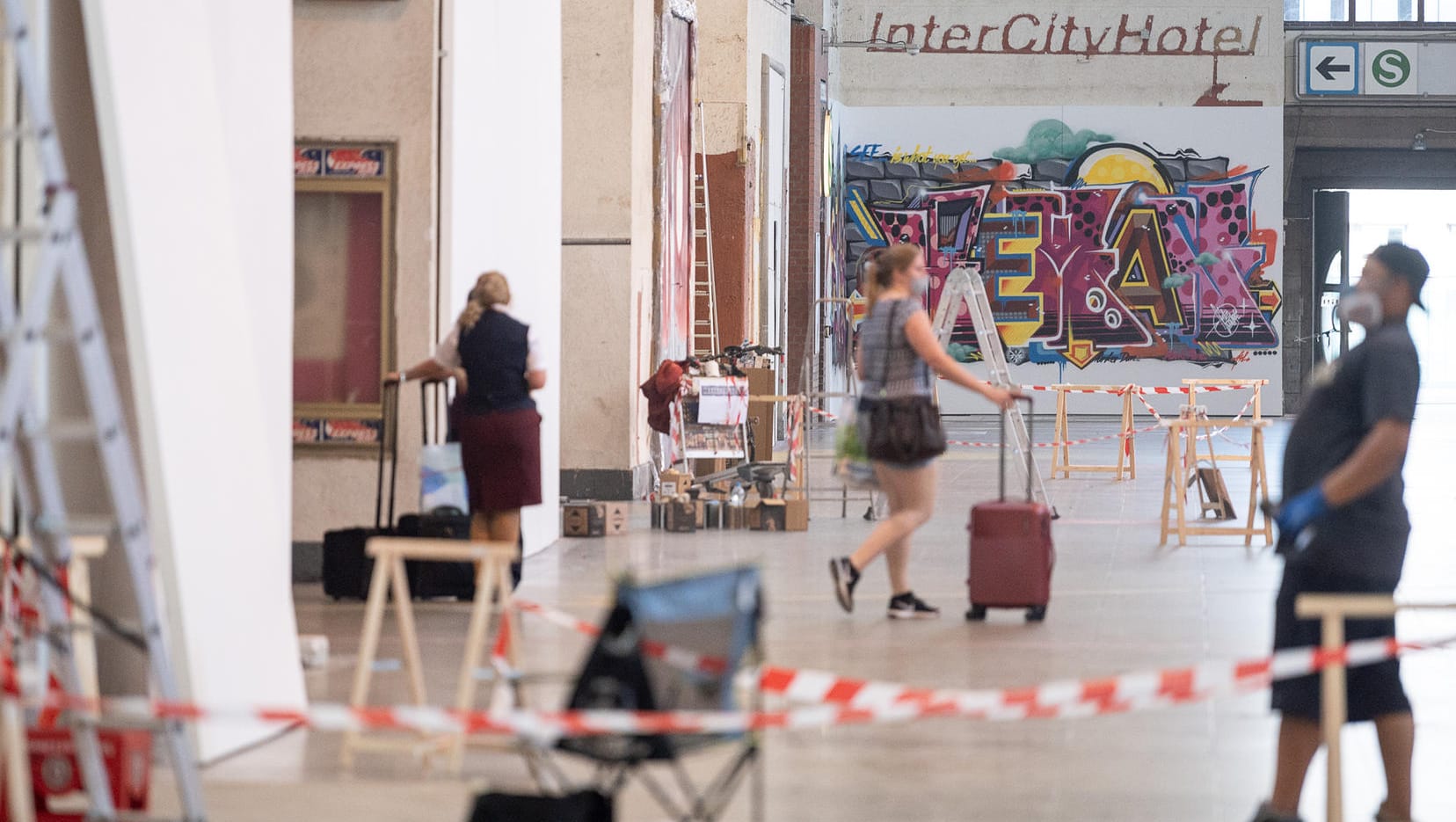 Personen gehen durch die Halle des Hauptbahnhofs: Im Hintergrund hängt ein Werk.