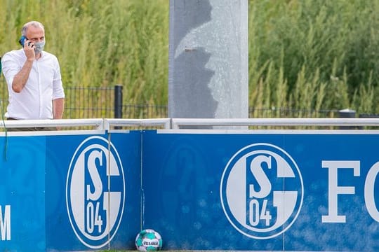 Schalkes Sportvorstand Jochen Schneider steht beim Training hinter einer Bande und telefoniert mit seinem Handy.