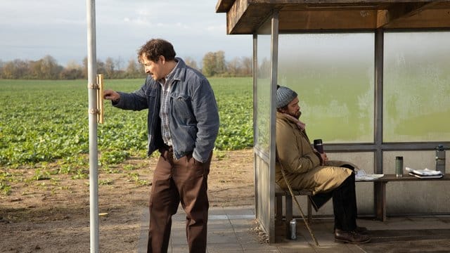 Ralf (Felix Kramer) studiert den Busfahrplan, Johannes (Ronald Zehrfeld) sitzt in der Bushaltestelle.