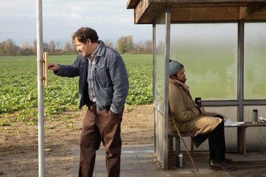 Ralf (Felix Kramer) studiert den Busfahrplan, Johannes (Ronald Zehrfeld) sitzt in der Bushaltestelle.