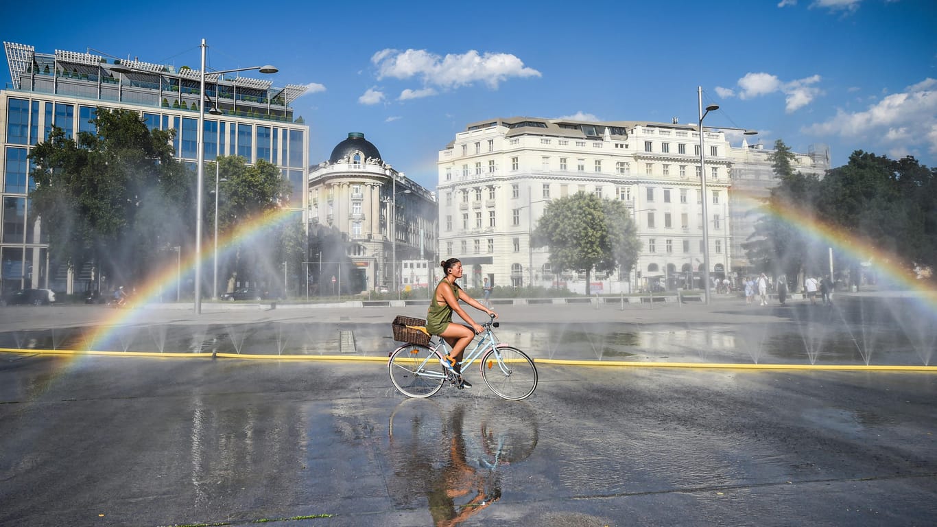 Österreich, Wien: Ein Radfahrerin kühlt sich in der Nähe einer Wasserinstallation auf dem Schwarzenbergplatz ab. Die österreichische Hauptstadt hatte in diesem Jahr bereits Temperaturen von bis zu 37 Grad.