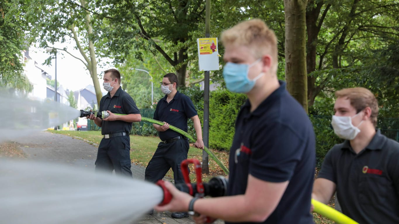 Feuerwehrleute richten Wasserschläuche auf Bäume in Wuppertal: Die große Hitze macht den Bäumen in der Stadt zu schaffen.