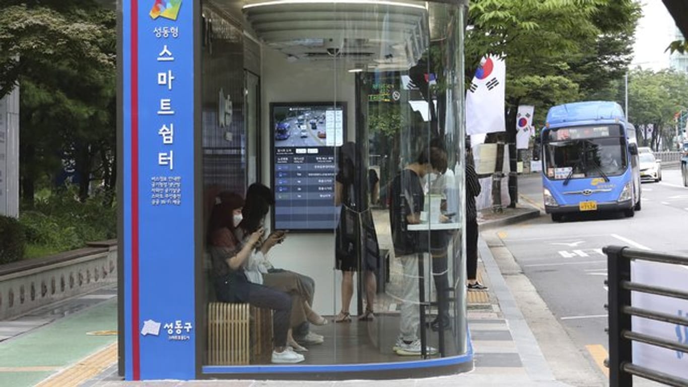 Menschen warten in Seoul in einem "smarten" Wartehäuschen auf den Bus.