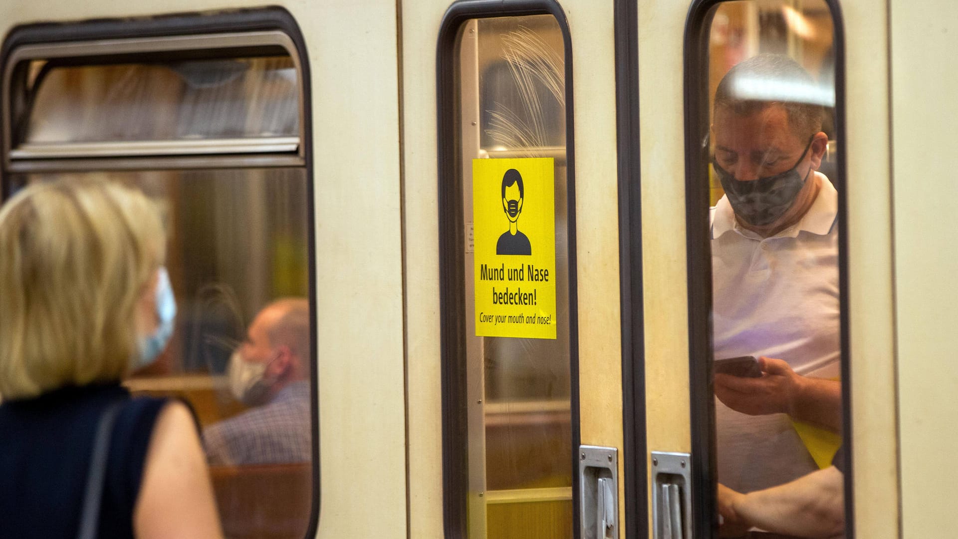 "Mund und Nase bedecken" auf einem Schild (Symbolbild): Fahrgäste tragen eine Alltagsmaske. "Mund und Nase bedecken" auf einem Schild (Symbolbild): Fahrgäste tragen eine Alltagsmaske.