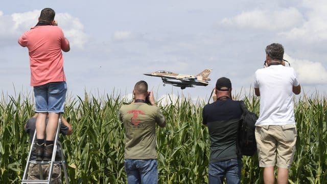 Ein israelischer F-16 Bomber landet auf dem Fliegerhorst Nörvenich im Kreis Düren, beobachtet von mehreren Männern mit Kameras, die an einem Maisfeld stehen.